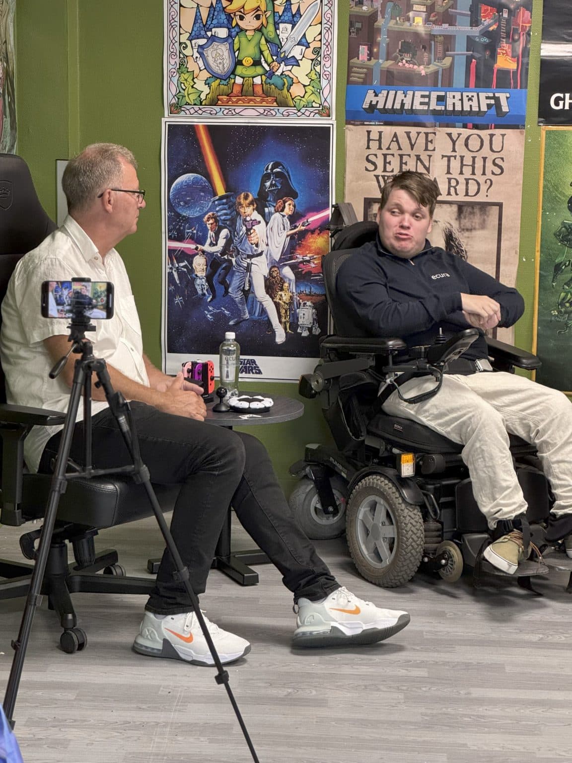 To personer i samtale foran kamera i gamingrom med plakater fra Zelda, Star Wars, Minecraft og Harry Potter – et bilde på digital kultur og inkludering.